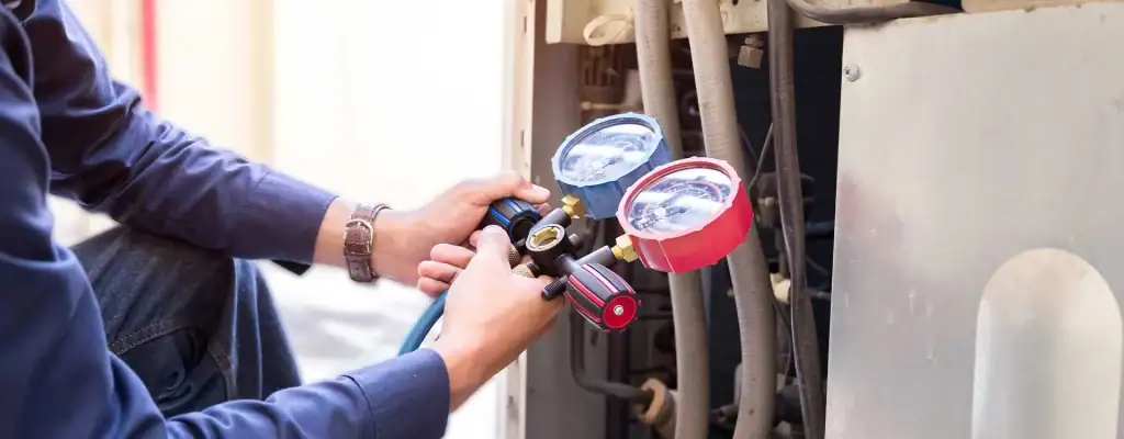 A person uses HVAC gauges to check the pressure on an air conditioning unit, adjusting the controls and inspecting the connected pipes and tubing.